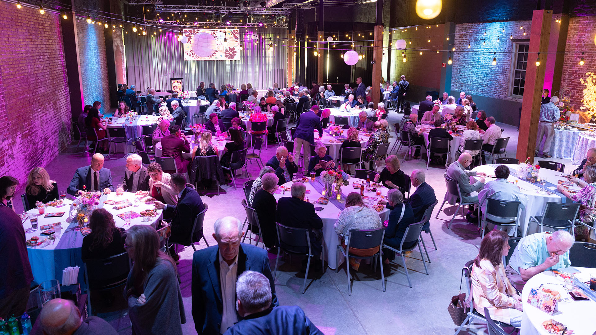 A room full of people dining and socializing at The Old Glass Place during the Medallion Reception.