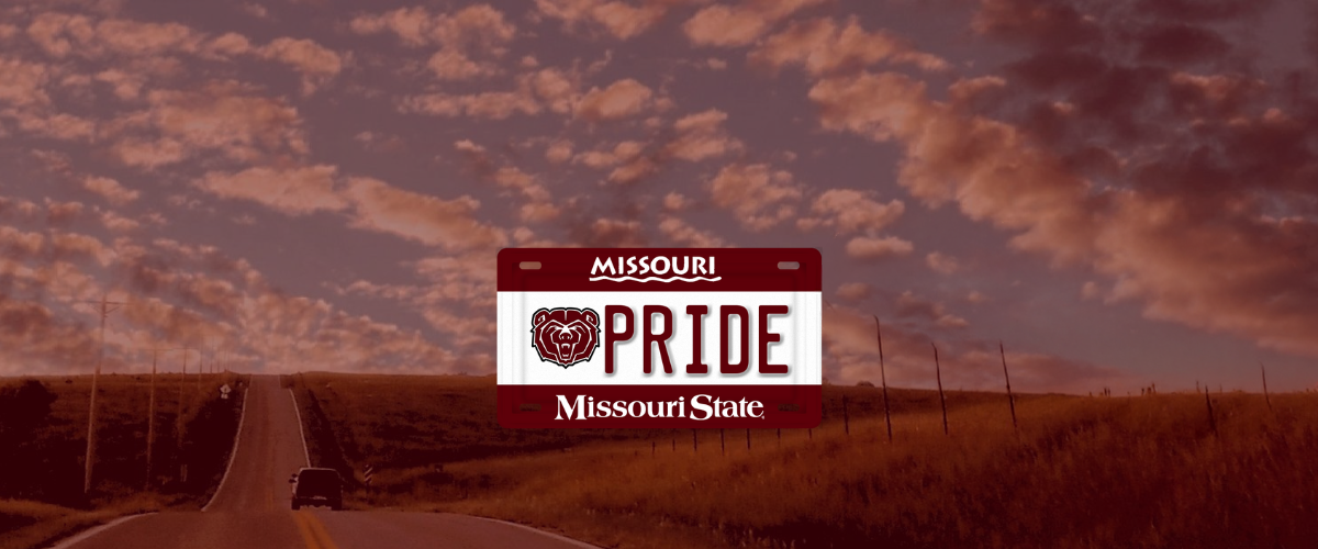 Photo of a rural highway surrounded by fields under a partly cloudy sky with an example maroon and white Missouri State license plate featuring a bear head and Pride on it layered over the top